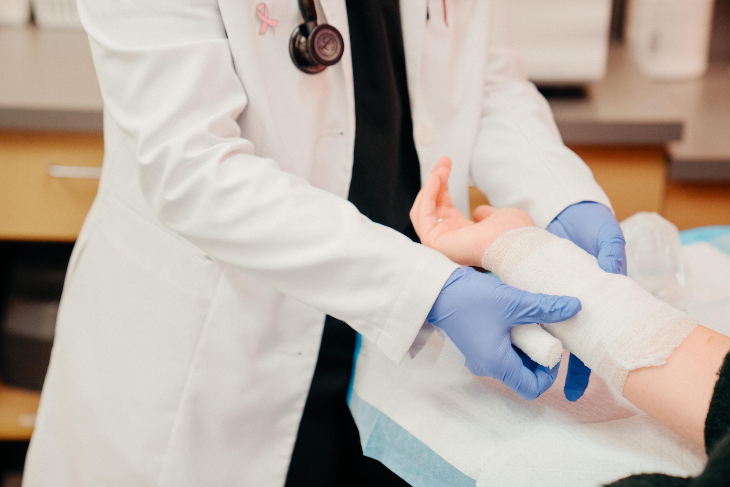 AFC healthcare provider wrapping a patient’s lower right arm in bandage after experiencing a burn or rash.