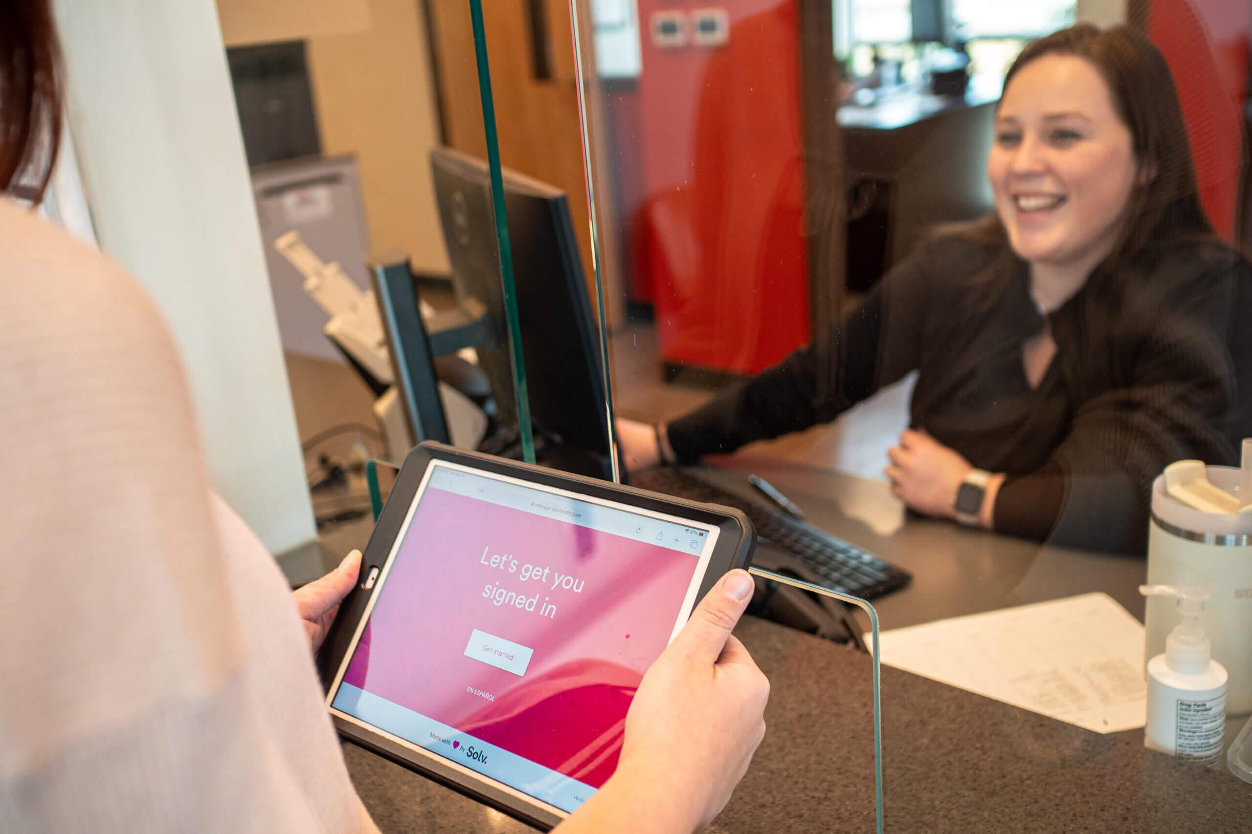 Female patient checking in to an AFC clinic with the receptionist greeting her with a friendly smile.