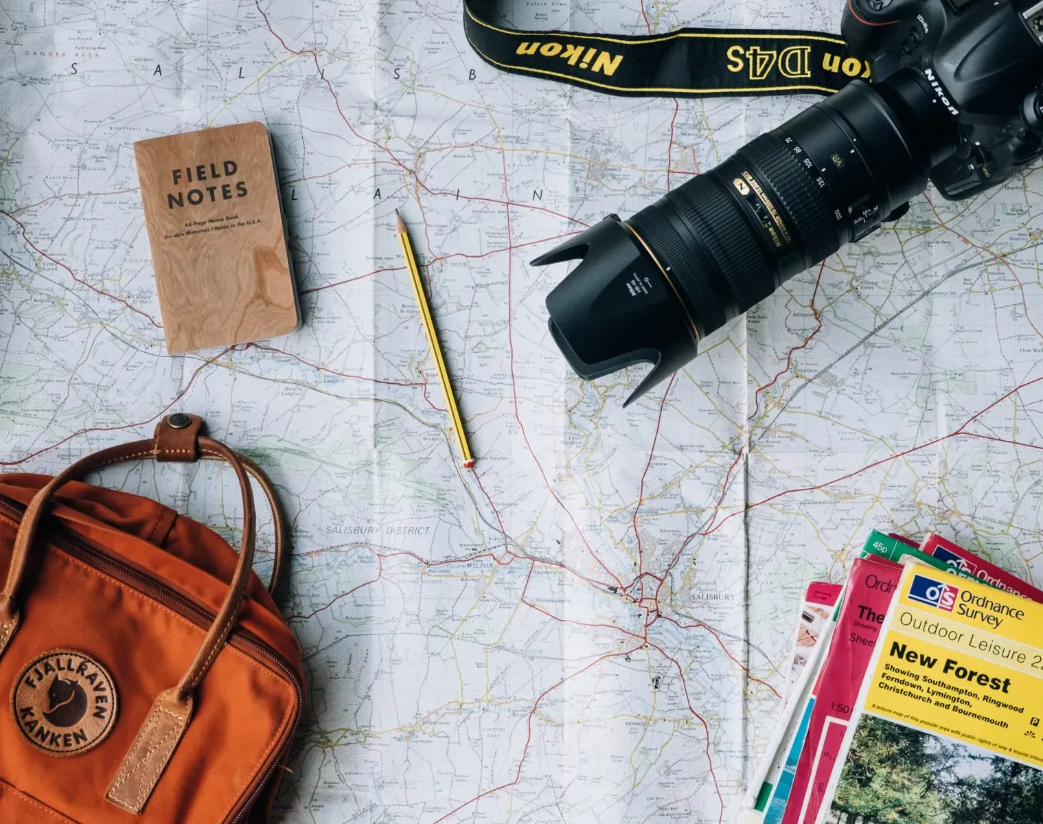 A map with a travel bag, camera with notes and a pencil sitting on top