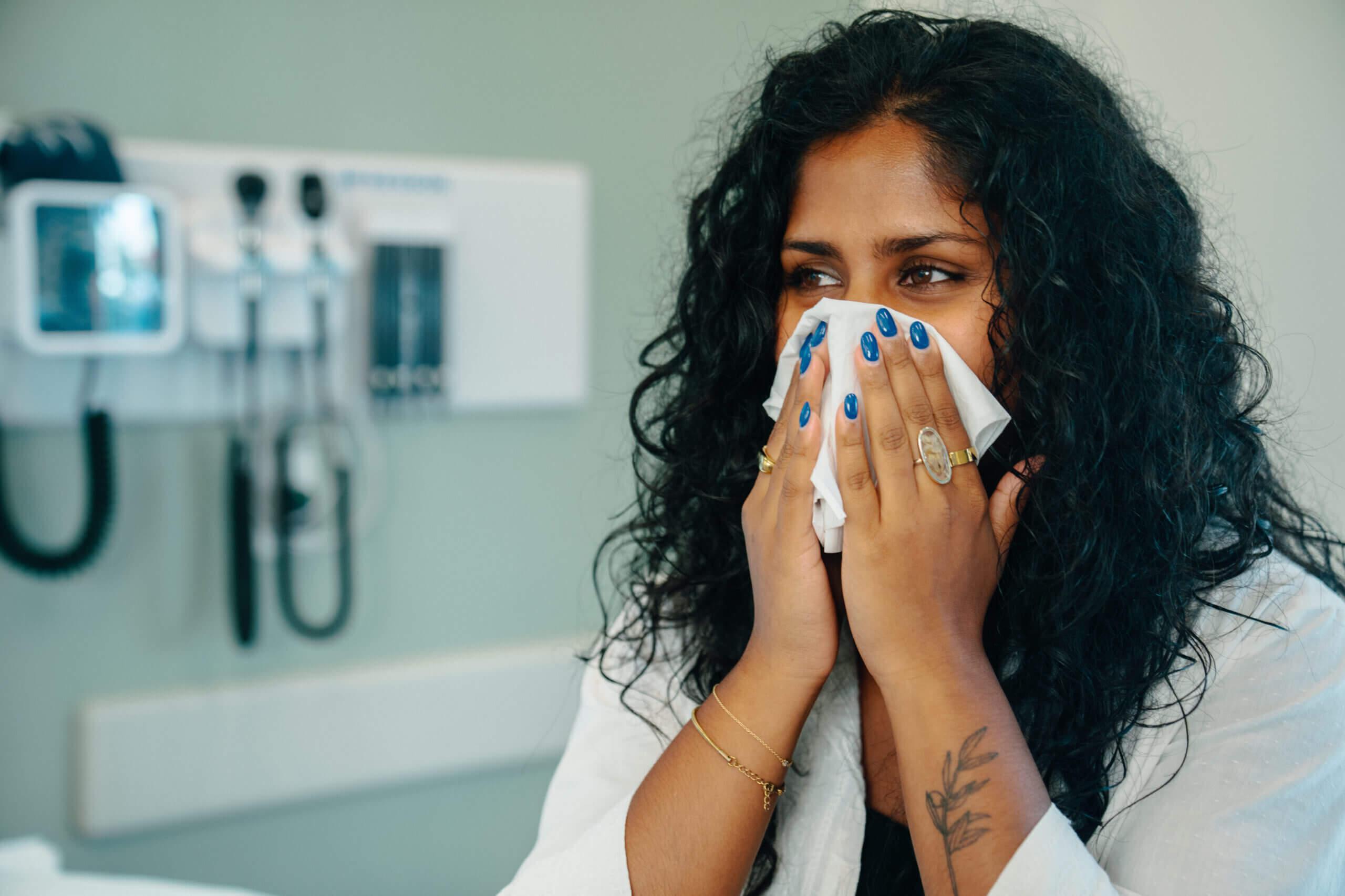 Patient in an AFC examination room blowing her nose due to symptoms from a sinus infection.