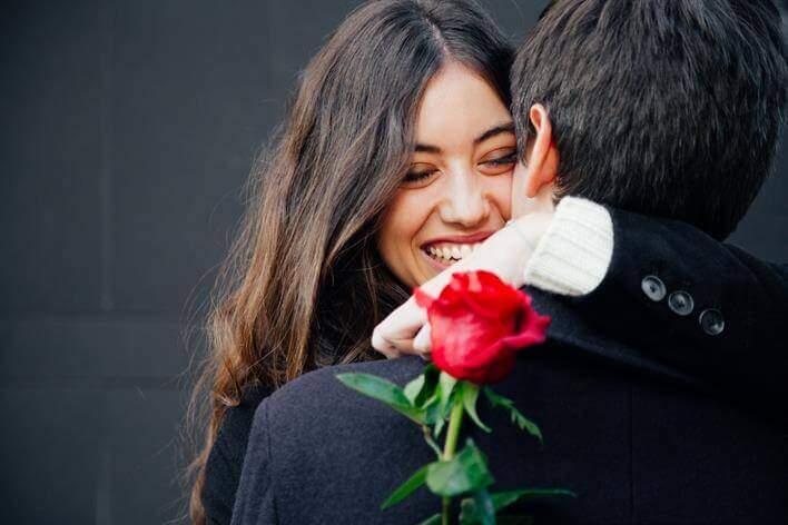 A smiling woman embraces a man while holding a red rose, just outside the walk in clinic.