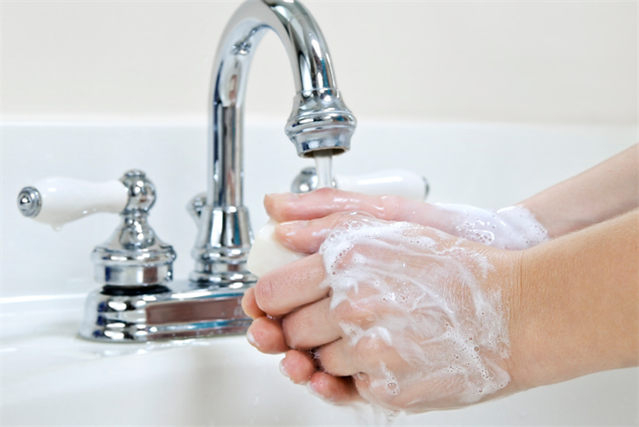 Person washing hands with soap under a chrome faucet in a white sink, as commonly seen in a medical center.