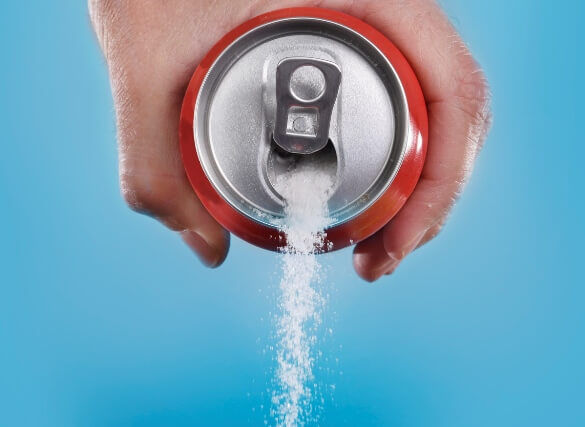 A hand pours a large amount of sugar from a soda can against a blue background, highlighting the hidden dangers often discussed at your local medical center.