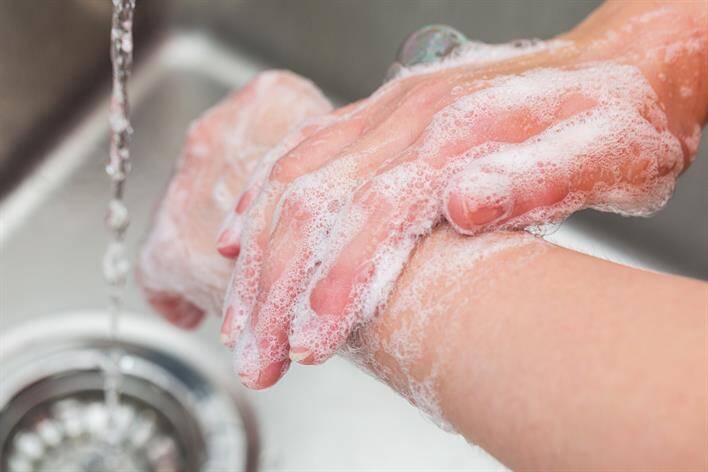 A person is washing hands with soap under running water in a sink at a medical center.