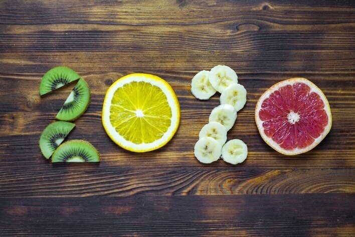 The year "2020" is creatively spelled out using slices of kiwi, orange, banana, and grapefruit on a wooden surface, resembling the fresh and healthy options often available at a medical center's wellness program.