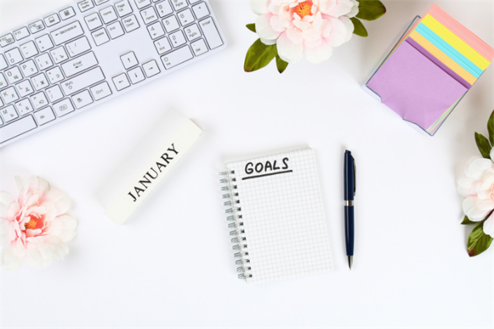 A keyboard, sticky notes, pen, and flowers surround a notepad labeled "Goals" and a block with "January" written on it—a serene workspace that could easily be found in a medical center's staff room.