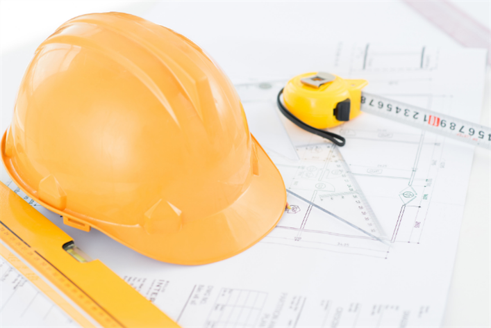 Yellow hard hat, measuring tape, and triangular ruler rest on architectural blueprints for a new medical center.