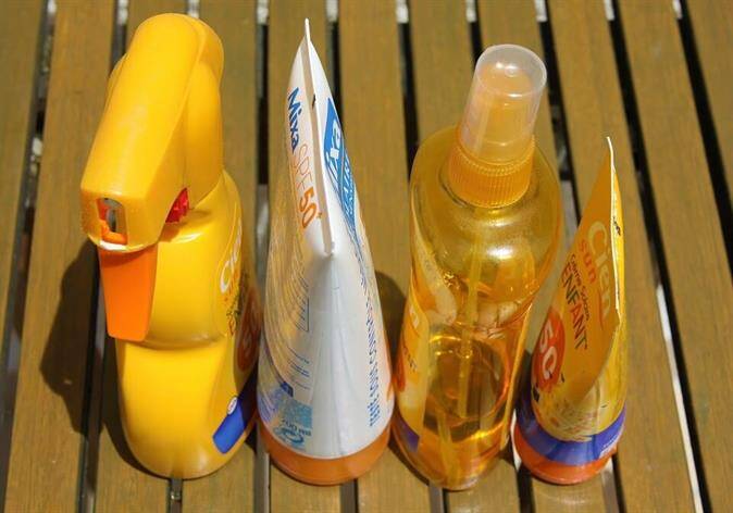 Four bottles of sunscreen, including spray and squeeze types, are arranged in a row on a wooden surface—perfect for anyone visiting the beach or a walk-in clinic.
