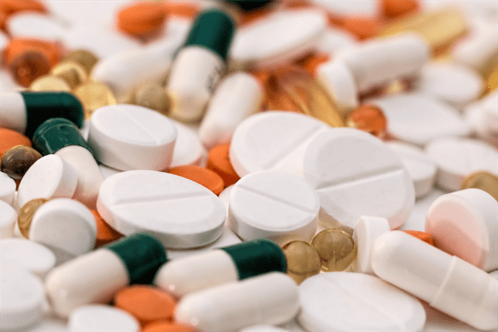 A close-up of various pills and capsules in different shapes, sizes, and colors—including white tablets, green and white capsules, and orange and clear gel capsules— reminiscent of what you might find in a medical walk-in clinic or urgent care setting.