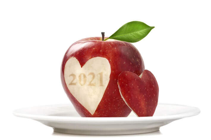 A red apple with "2021" and a heart shape carved into it sits on a white plate, reminiscent of the precision found in a medical center. A smaller, carved-out heart piece of the apple is placed next to it.