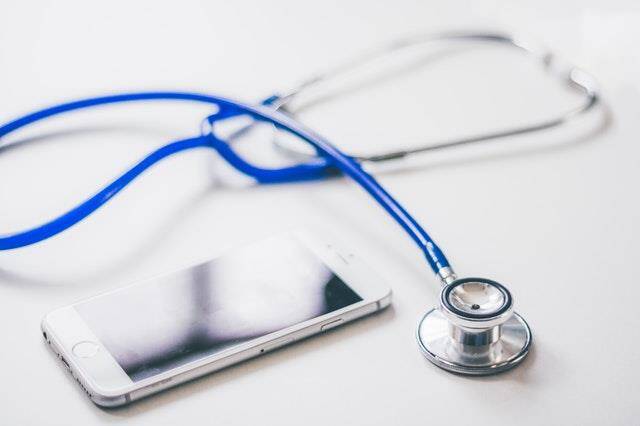 Close-up of a stethoscope and a smartphone placed next to each other on a white surface, symbolizing the blend of traditional medical tools with modern technology in urgent care.