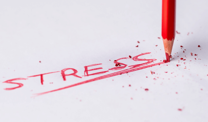 Close-up of a red pencil underlining the word "STRESS" written on white paper, with pencil shavings scattered around, evocative of the tension often relieved at a walk-in clinic.