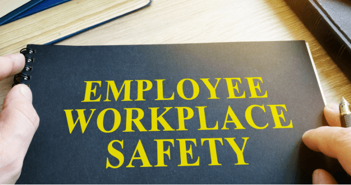 Hands holding a booklet titled "Employee Workplace Safety" on a wooden desk, ideal for staff at the medical center.