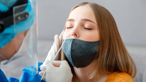 At a medical center, a healthcare professional wearing gloves and protective gear administers a nasal swab test to a woman wearing a mask.