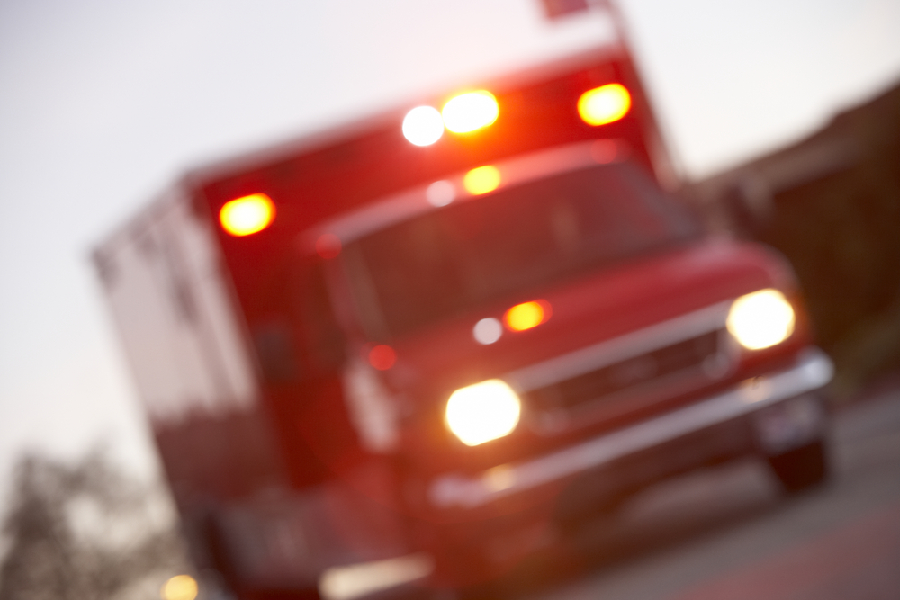 A blurred image of a red ambulance with lights on, suggesting it is responding to an urgent care emergency.