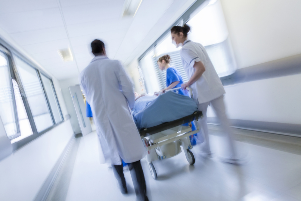 Medical staff from American Family Care in a hospital corridor are pushing a patient on a gurney.