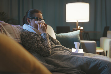A woman blowing her nose because she is sick and doesn’t know if it’s flu, RSV or something else