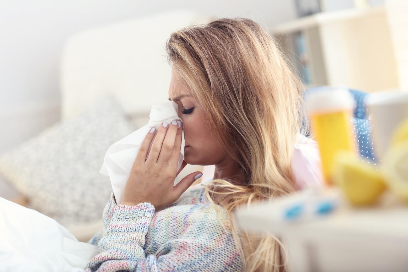 Woman blows her nose from flu, cold, or COVID-1S symptoms