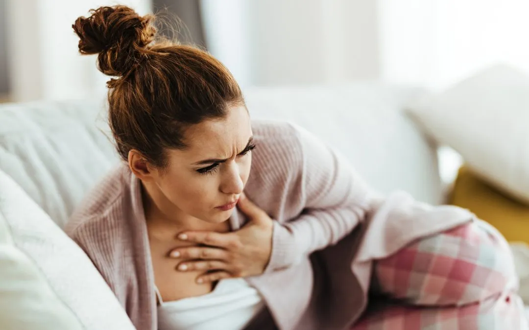 Young woman feeling chest pain while lying down on sofa at home
