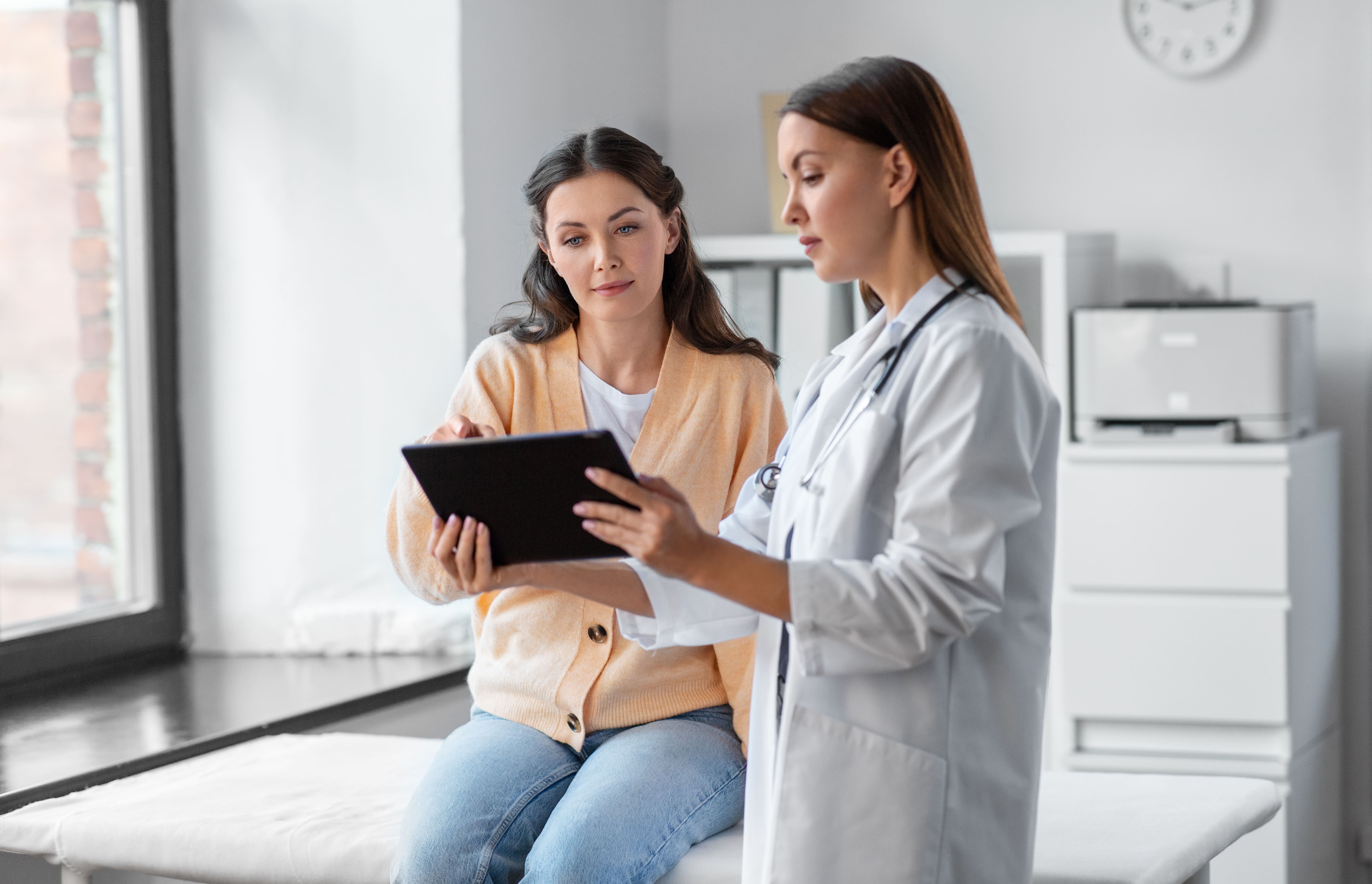 female doctor with tablet talking to woman patient at hospital